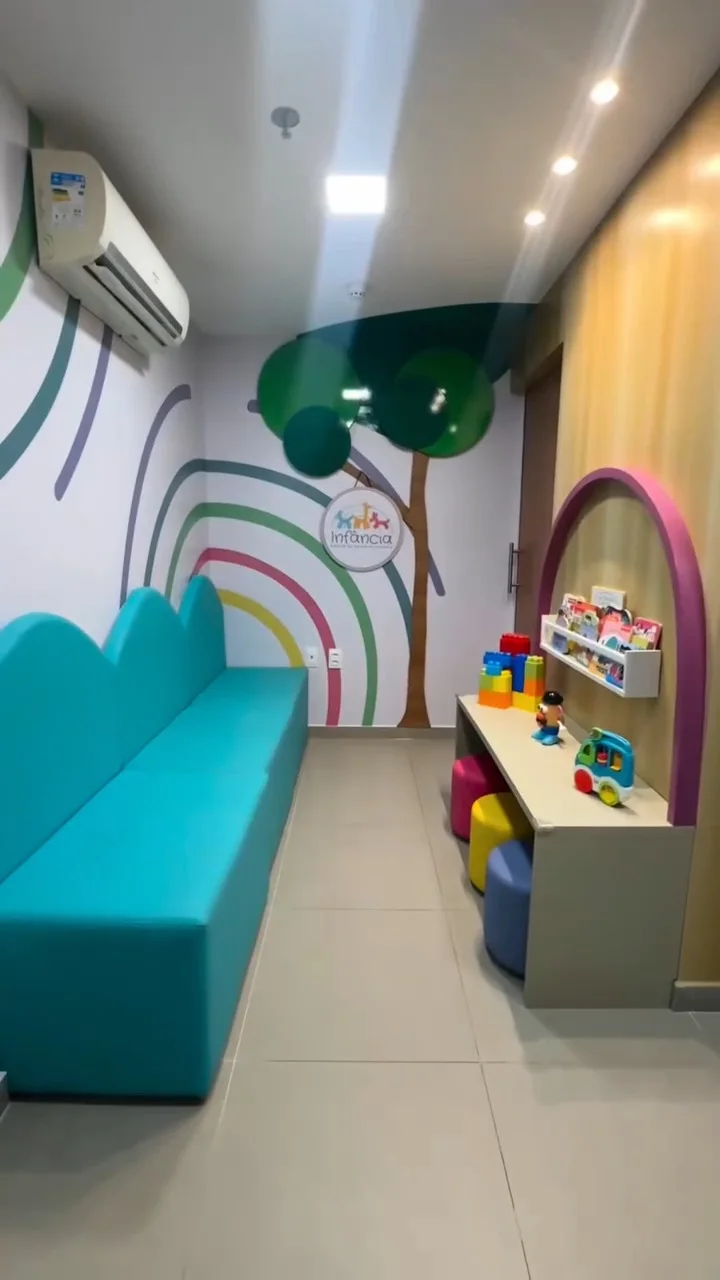 Recepção da Clínica Infância, com sofá azul, arco-íris pintado na parede e brinquedos